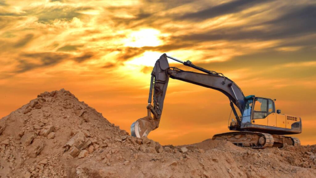 A digger on a mound of dirt in front of a sunset