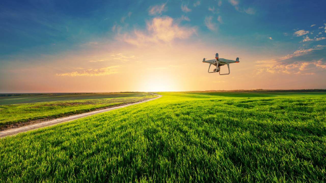 Smart digital farming drone flying over a crop field as the sun sets