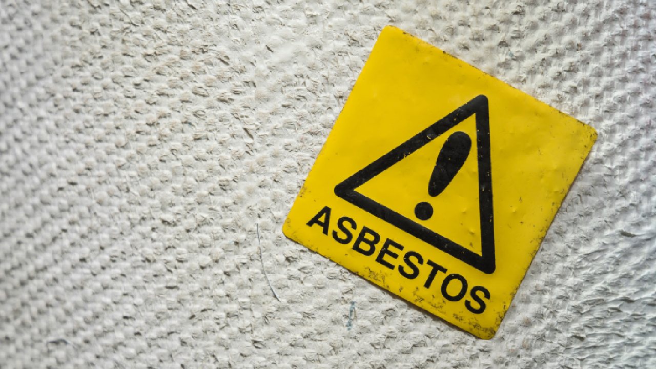 Why Asbestos Is Still Being Missed—Even When Testing Exists 1 Warning sign labelled “Asbestos” placed on a textured asbestos-containing surface, highlighting asbestos contamination and health risk awareness.